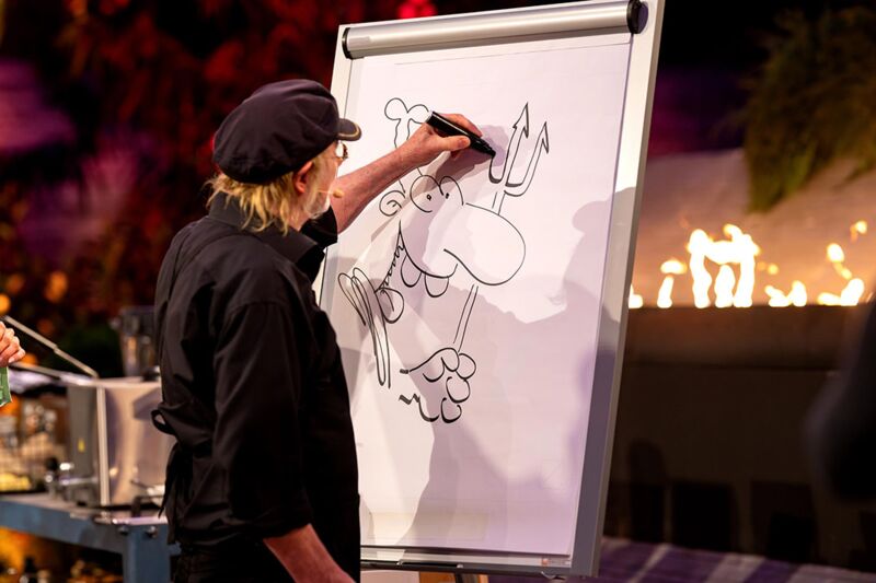 Brösel zeichnet Werner auf ein Flipchart, im Hintergrund das Kochstudio